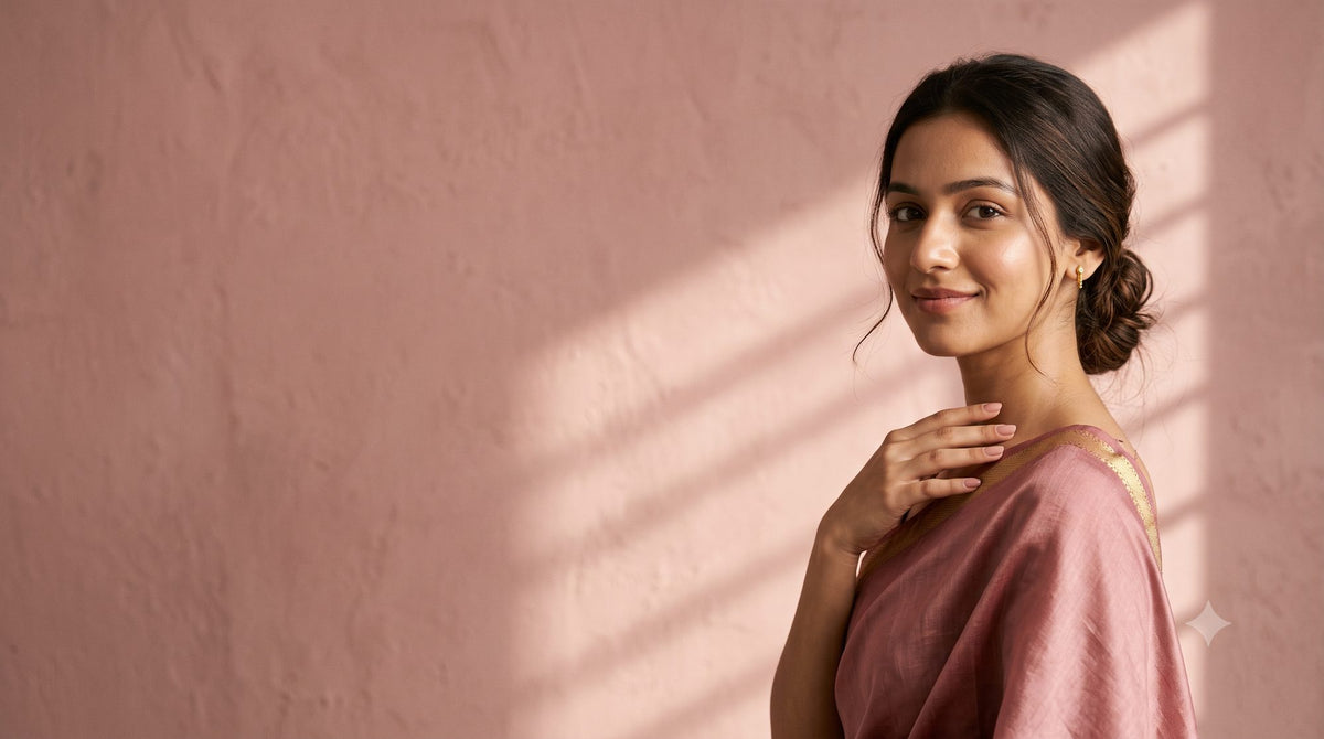 A young woman in a dusty-rose silk saree with a gold zari border, smiling