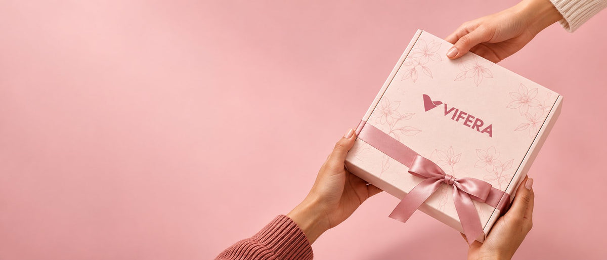 Two hands passing a pink VIFERA gift box tied with a satin ribbon